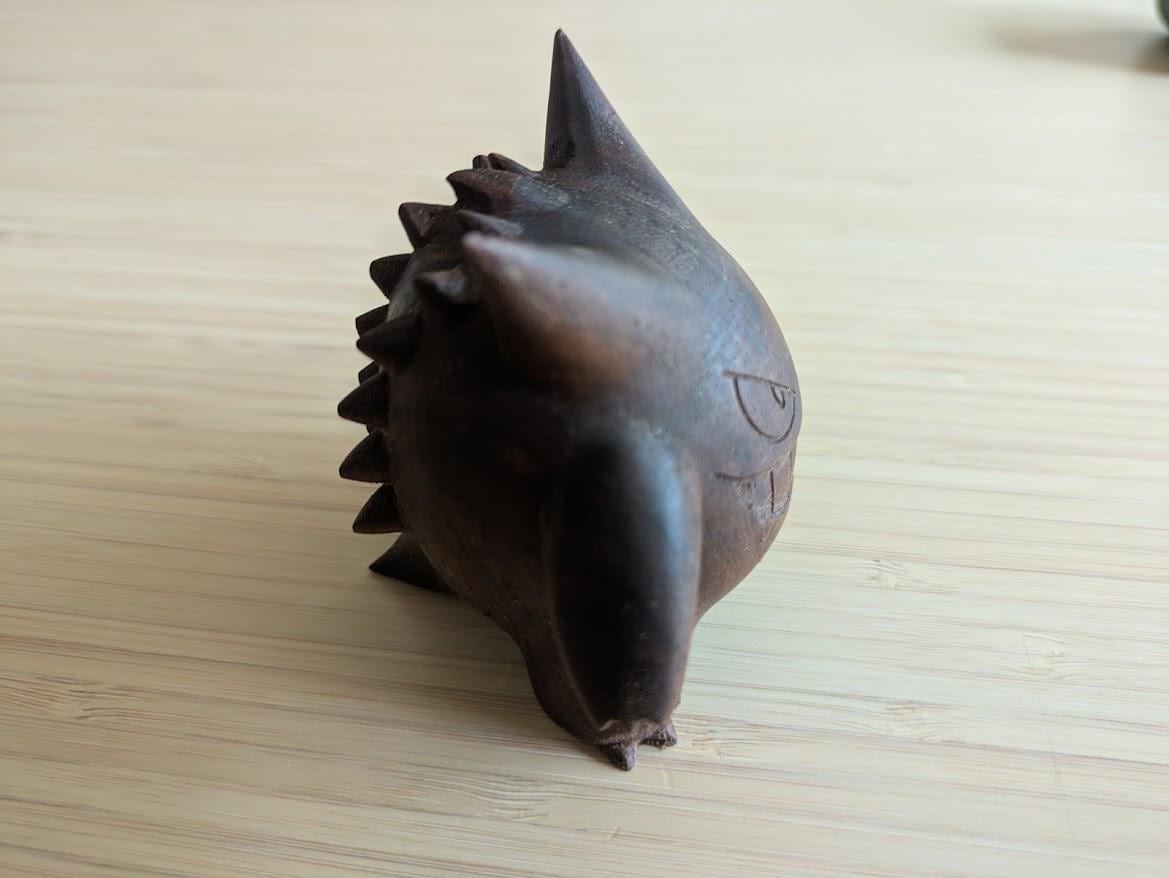 Dark brown ceramic or clay sculpture of a creature with spikes 