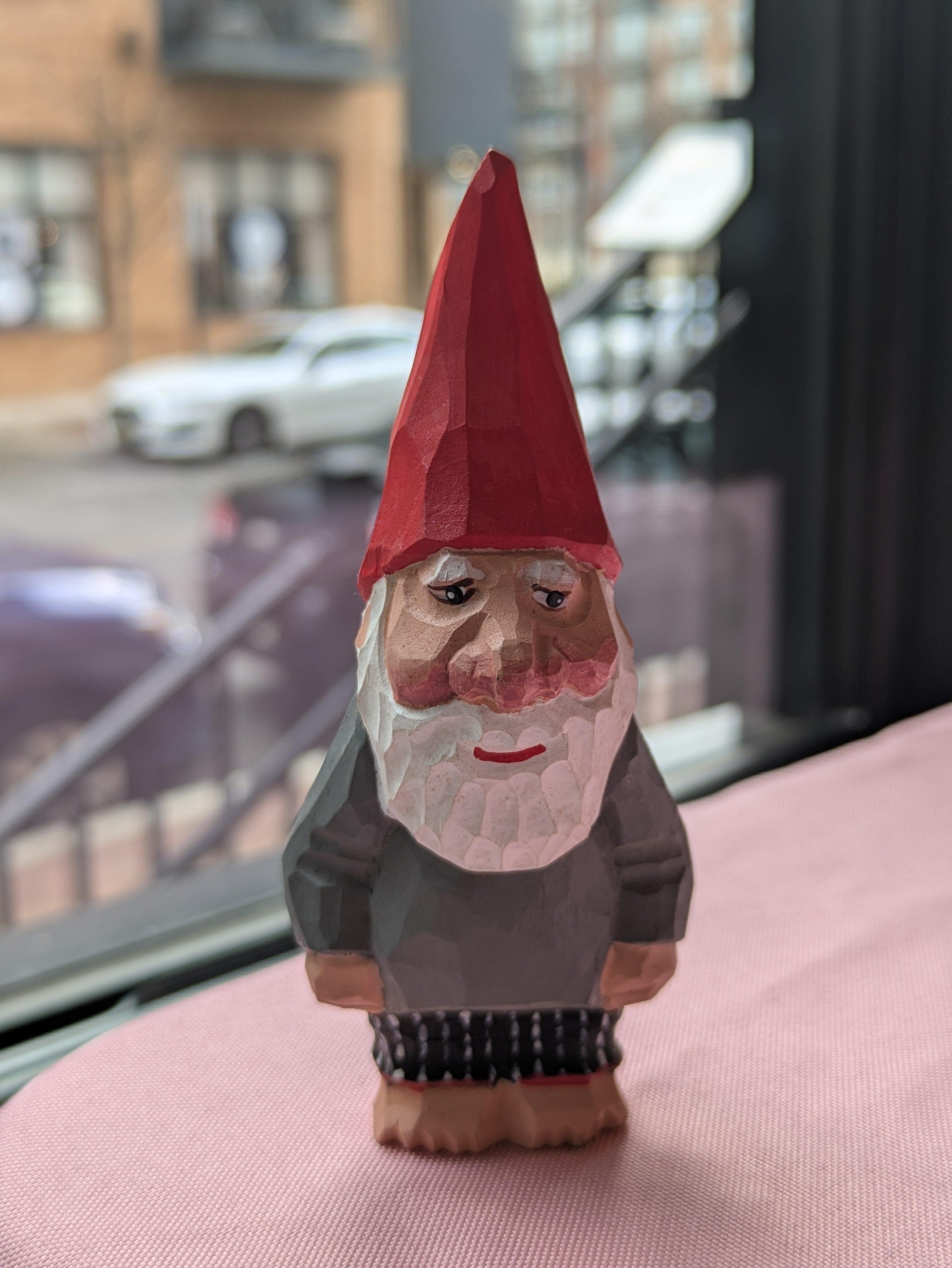 Wooden gnome figurine with a red hat on a pink surface