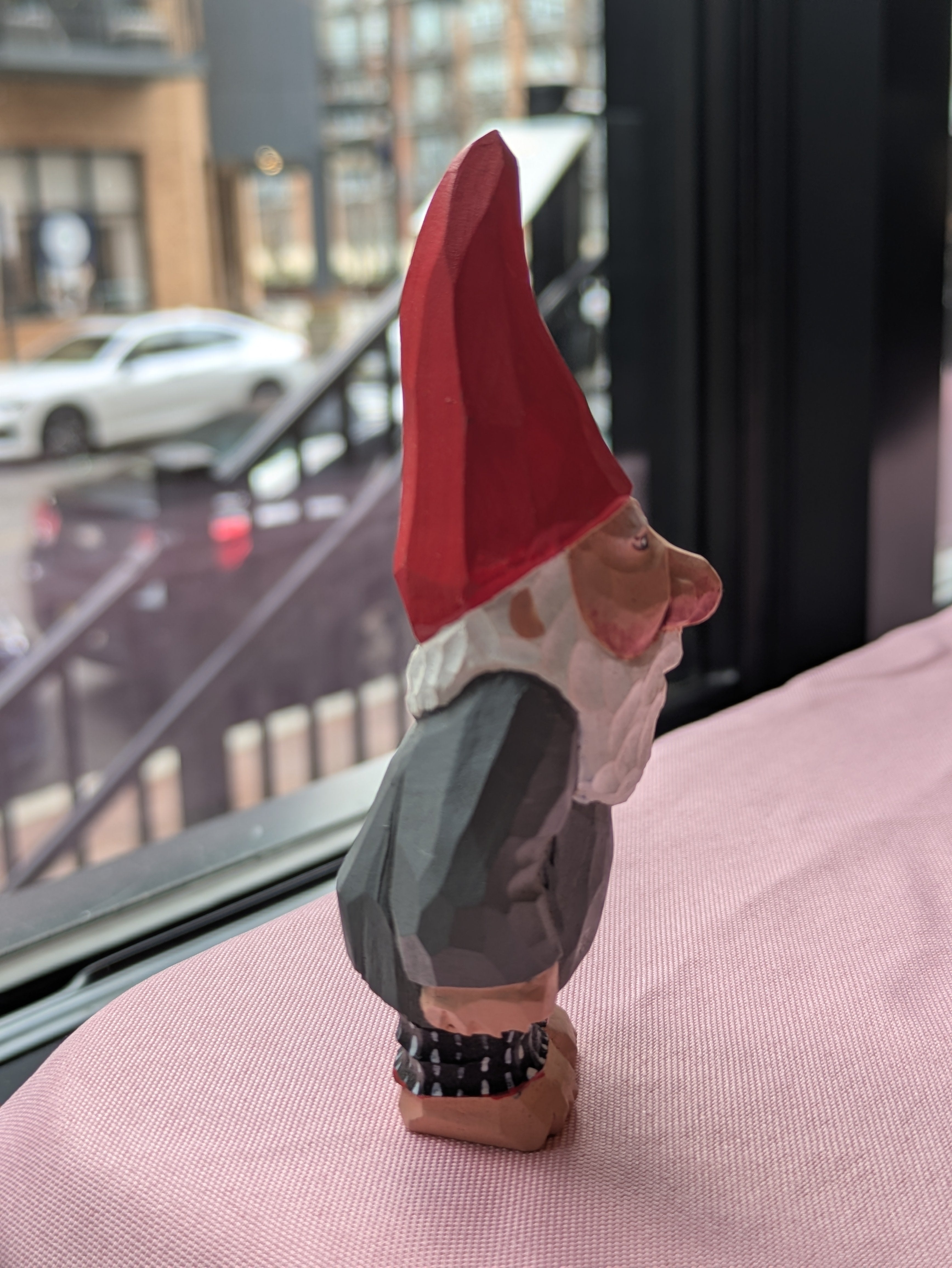 Gnome figurine with a red hat on a pink surface 