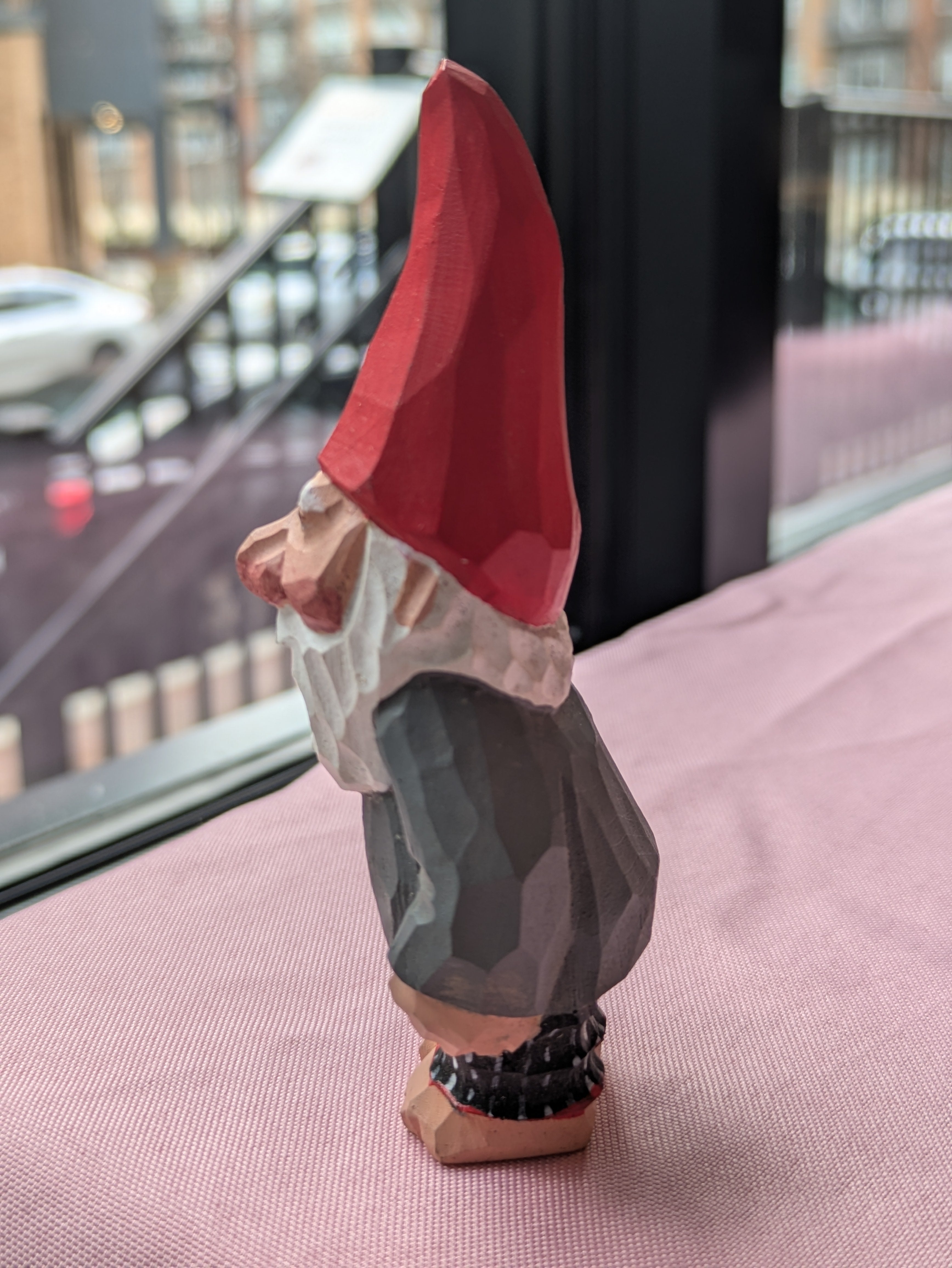 Gnome figurine with a red hat on a pink surface 