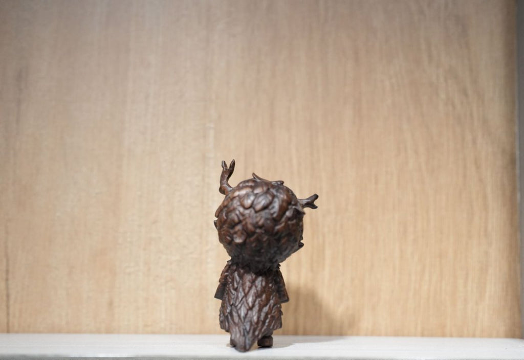 Bronze sculpture of a figure with a textured head on a wooden surface