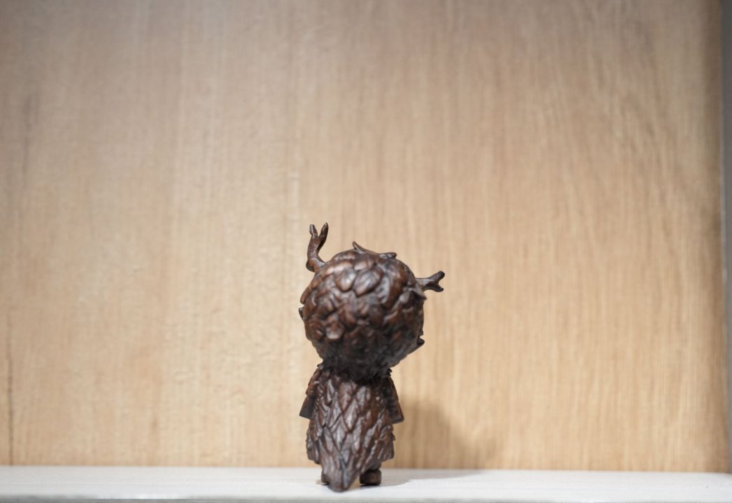 Bronze sculpture of a figure with a textured head on a wooden surface