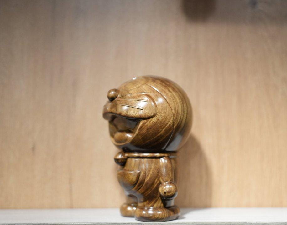 Wooden sculpture of a character with a round head and cylindrical body on a wooden background